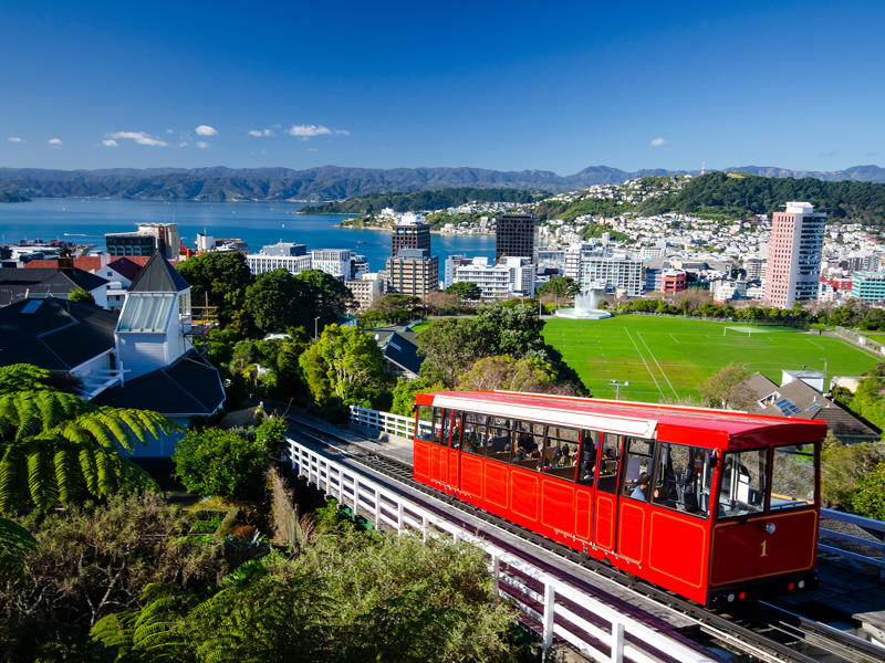 un tramway rouge sur une voie avec le téléphérique de Wellington et de l’eau en arrière-plan