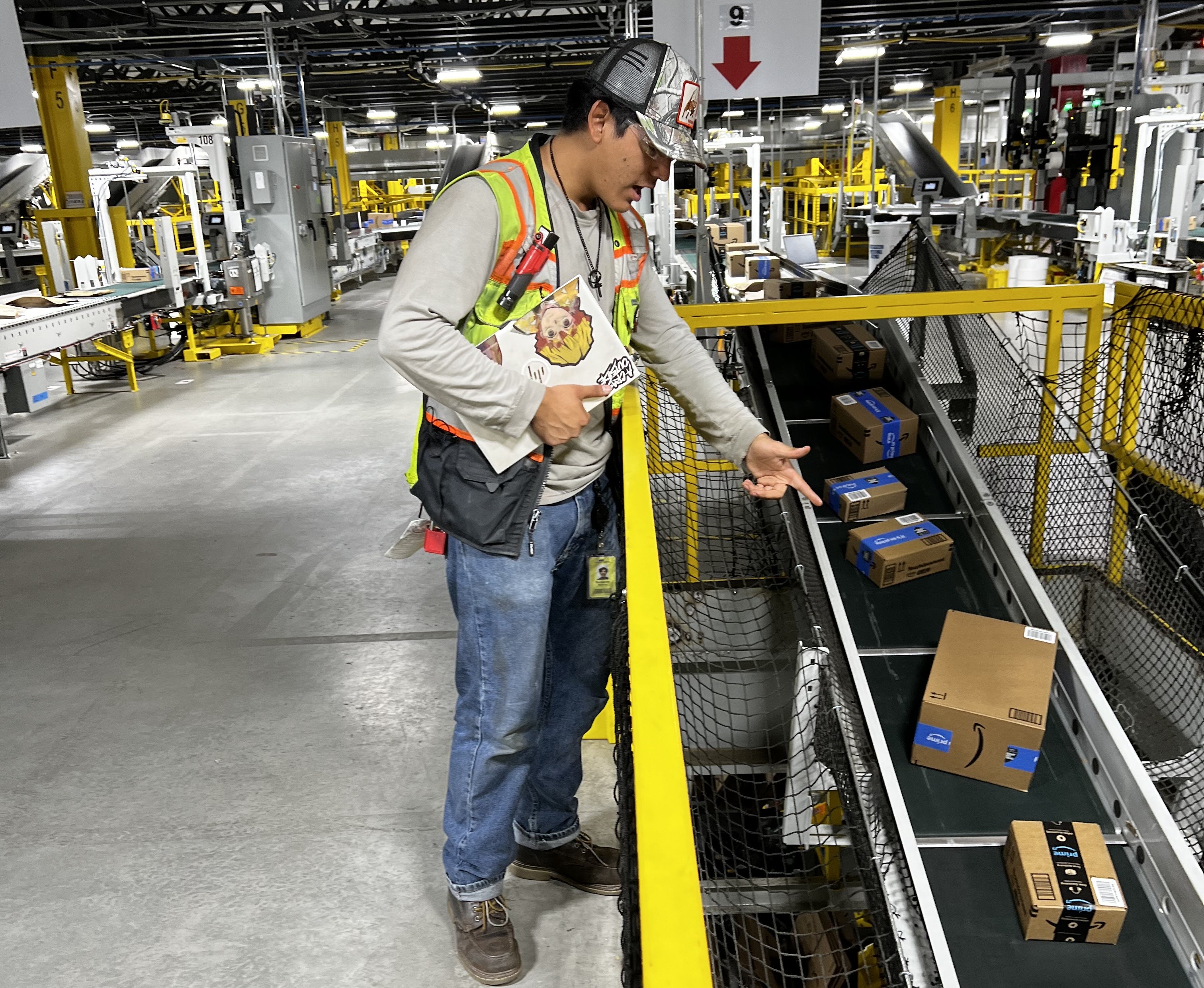 a person in a vest pointing at boxes on a conveyor belt