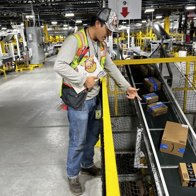 a person in a vest pointing at boxes on a conveyor belt