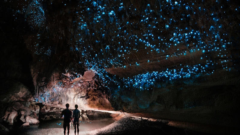 two people looking at glowing blue lights in a cave