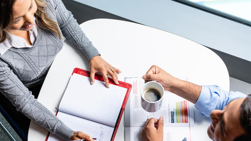 a person and person sitting at a table with a notebook and a cup of coffee