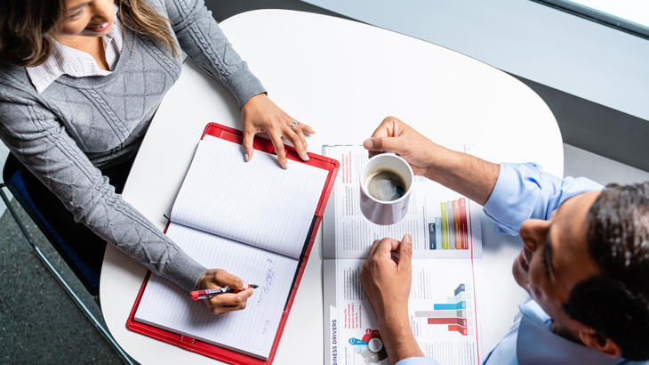 une personne et une personne assise à une table avec un cahier et une tasse de café