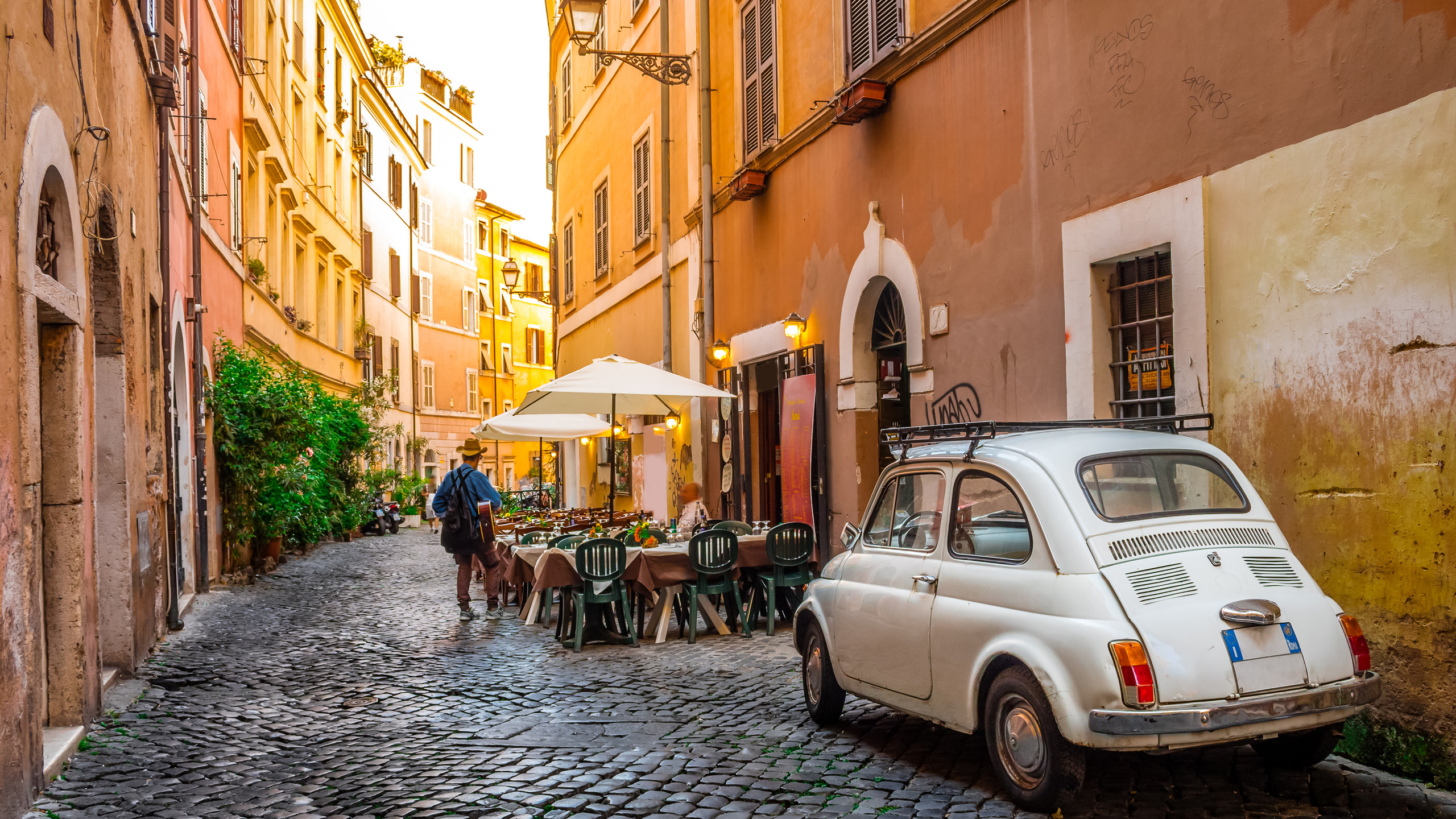 a person walking on a cobblestone street with tables and chairs