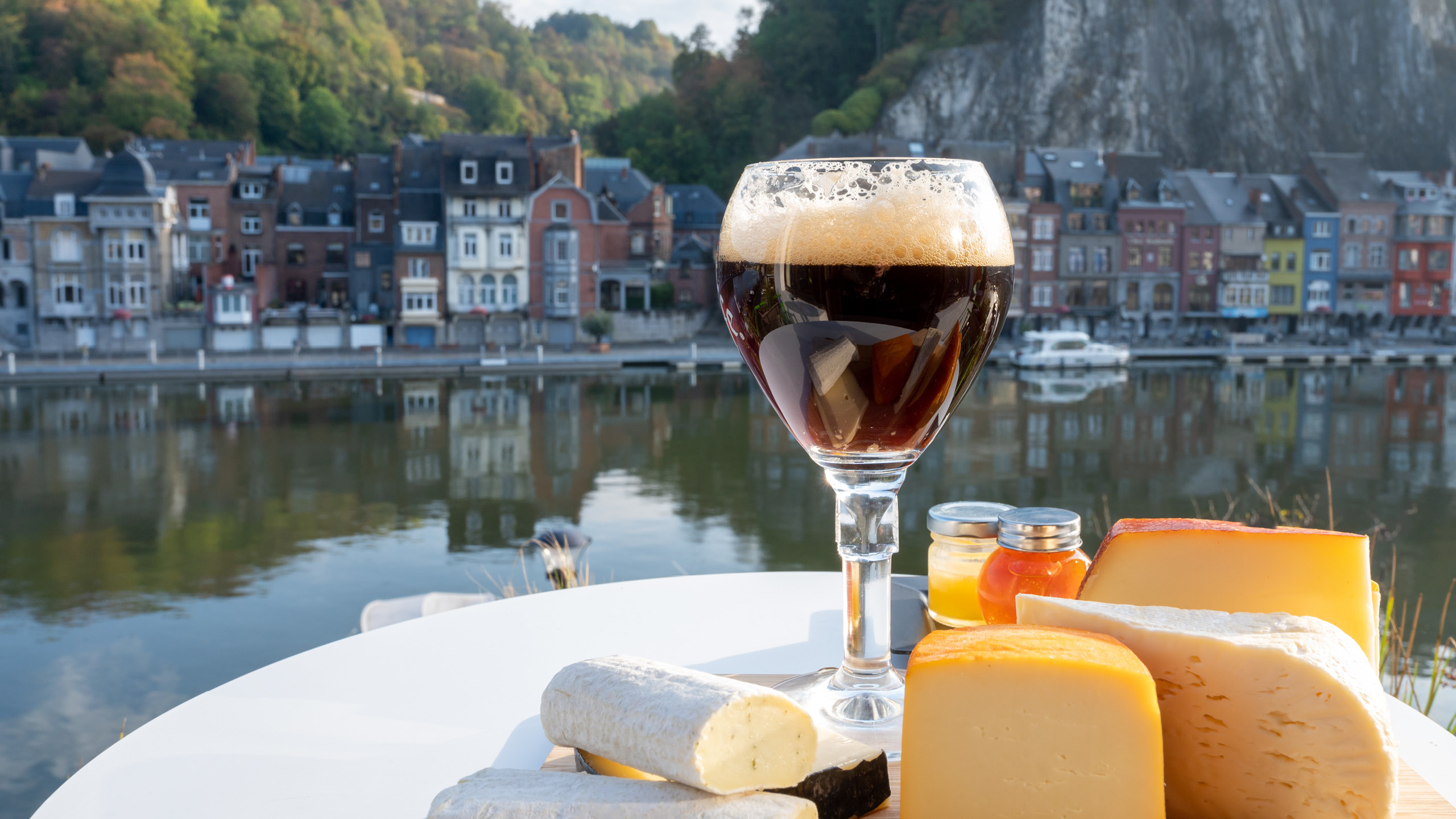 a glass of wine and cheese on a table with a river in the background